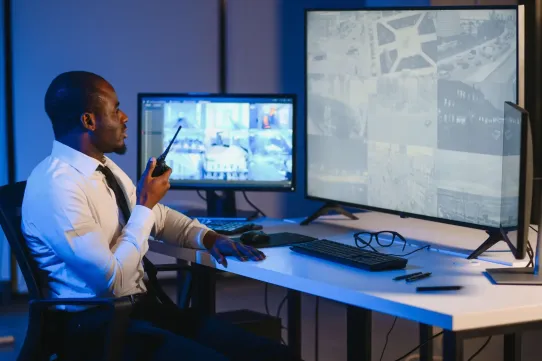 Security officer looking at monitors with two-radio in hand